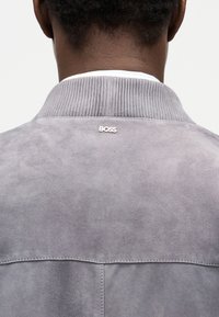 Οπίσθια όψη ενός ατόμου που φοράει ανοιχτό γκρι σουέντ μπουφάν με ριμπ γιακά και το λογότυπο "BOSS" κεντραρισμένο κάτω από το λαιμό.