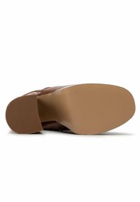 Suela de un zapato de vestir de cuero marrón que muestra una suela exterior de goma lisa y color canela y un tacón texturizado para tracción, fotografiado sobre un fondo blanco.