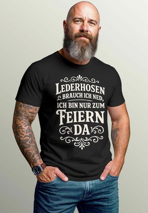 Schwarzes Baumwoll-T-Shirt mit weißem Drucktext und dekorativen Verzierungen. Kurze Ärmel, Rundhalsausschnitt, lockere Passform. Darunter werden Denim-Jeans getragen.