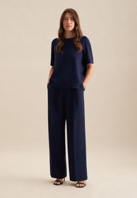 Top blu navy a maniche corte con vestibilità rilassata, abbinato a pantaloni a gamba larga. Tessuto liscio, senza motivi visibili, con tasche incluse.