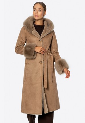 Bruine lange jas van suede met een met bont gevoerde capuchon en manchet. Voorzien van een strikceintuur en een sluiting met knopen aan de voorkant. Zachte textuur en neutrale tint.