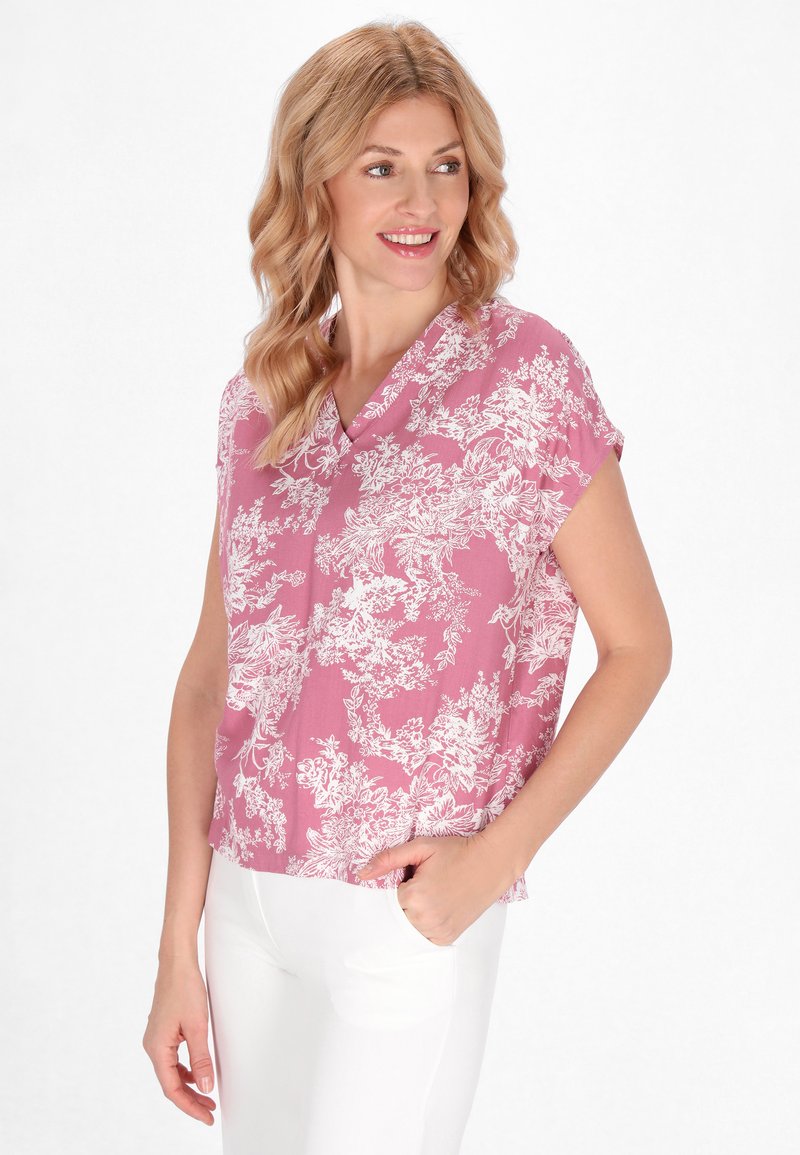 Blusa rosa a maniche corte con scollatura a V, caratterizzata da motivi floreali bianchi e una vestibilità morbida. Tessuto resistente alle pieghe.