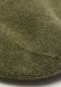 Tela verde tejida que muestra una textura suave y variaciones sutiles en el sombreado, con un borde redondeado y una apariencia ligeramente borrosa.