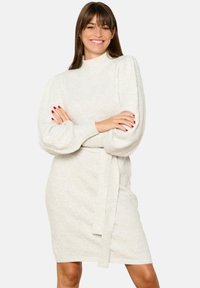 Knit dress in off-white with a high collar, balloon sleeves, diamond patterns, and a matching belt at the waist. Smooth texture.