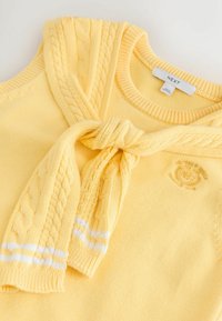 Pull en maille jaune douce avec une écharpe torsadée assortie drapée autour du cou, avec un discret logo brodé sur la poitrine.