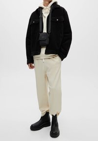 Giacca in corduroy nera sopra un hoodie crema, abbinata a pantaloni della tuta crema e stivali neri alla caviglia. Piccola borsa a spalla nera con tracolla.