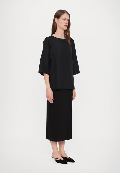 Zwarte oversized top met ruime mouwen, gecombineerd met een zwarte jurk tot de knie en zwarte pointy toe hakken. Gladde stof en minimalistisch ontwerp.