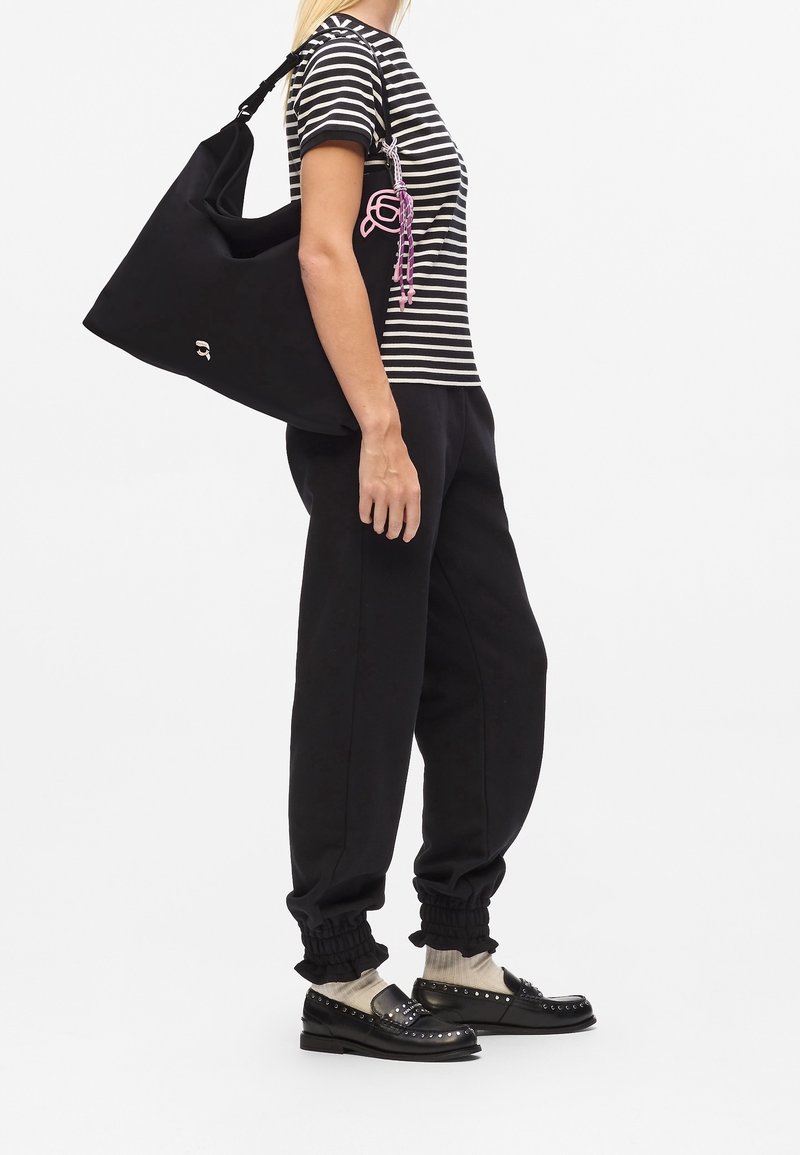 Femme portant une chemise rayée noire et blanche, un pantalon noir, des chaussettes beiges, des mocassins noirs cloutés, portant un grand sac à main noir.