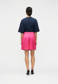 Μπλε ναυτικό κοντομάνικο μπλουζάκι συνδυασμένο με ροζ σορτς με ελαστική μέση. Τα σορτς έχουν ομαλή υφή και φτάνουν πάνω από το γόνατο. Μαύρα παπούτσια με τακούνι.