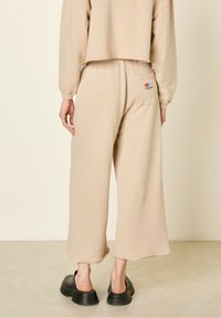 Beige brede sweatpants med et tekstureret stof, rå afslutning og et lille broderet logo på baglommen. Chunky sorte slip-on sko.