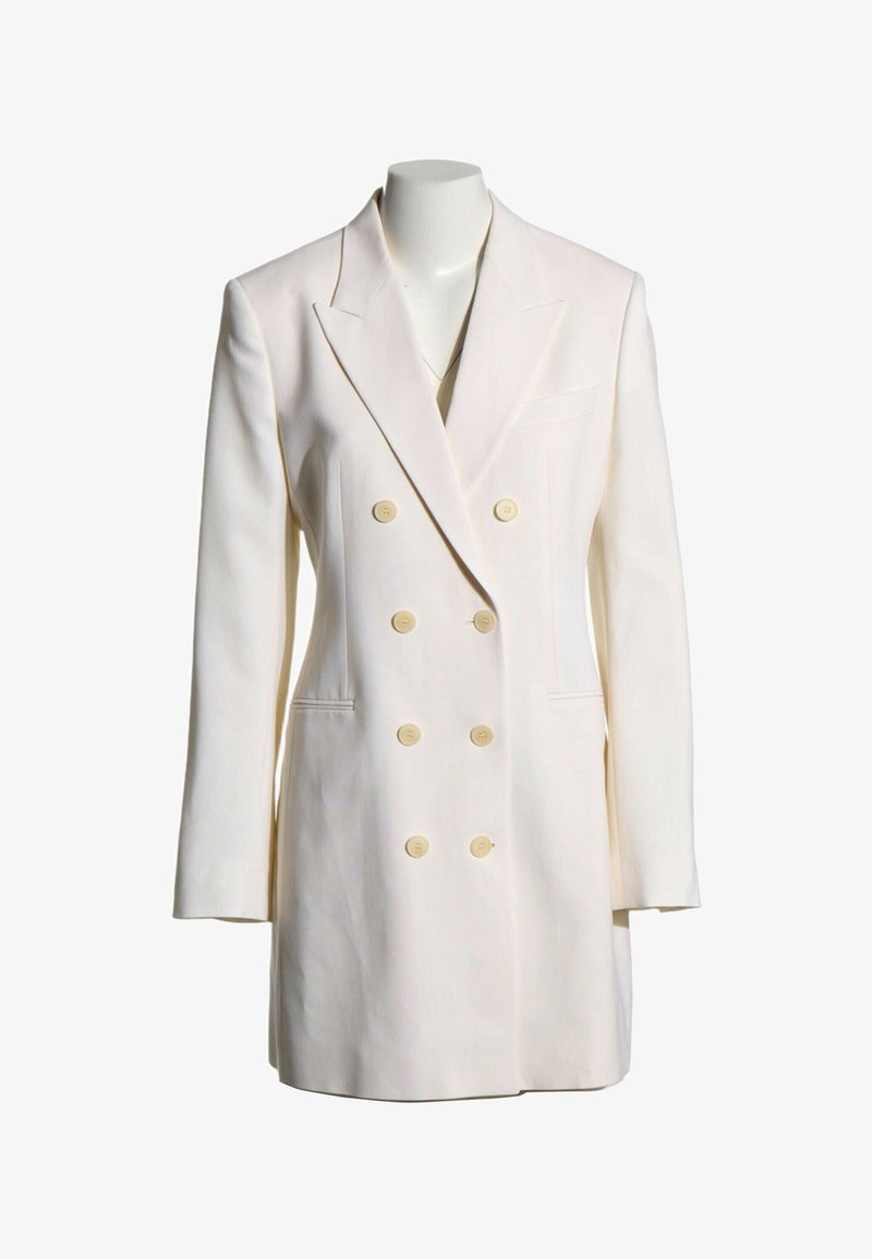 Blazer blanc croisé avec six boutons beiges, revers crantés, manches longues et deux poches avant sur un mannequin sans tête.