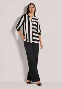 Gestreepte blouse in zwart en wit, met een mandarin-kraag en driekwartmouwen, gecombineerd met wijde zwarte broeken en open-toed hakken.