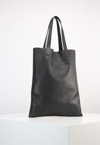 Sac cabas en cuir noir avec une finition texturée, doté de deux poignées robustes et d'une ouverture supérieure sans fermeture. Aucun élément décoratif ou matériel visible.