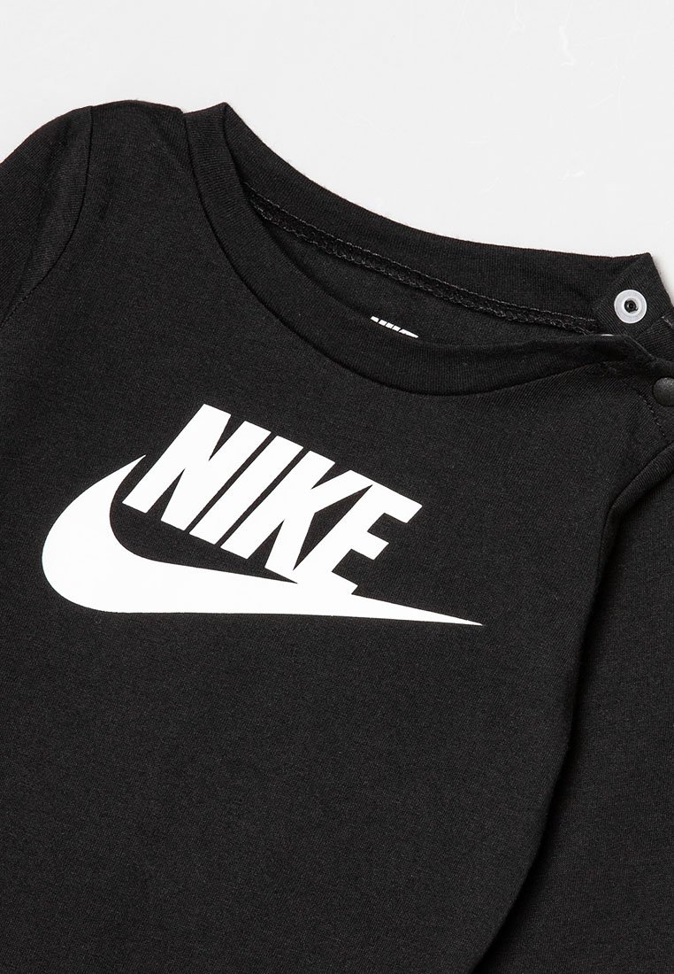 T-shirt en coton noir à col rond, arborant un grand logo Nike blanc sur le devant. Comprend des pressions aux épaules pour un enfilage facile.