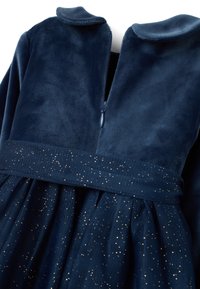 Abito blu navy con un morbido corpino in velluto e colletto, e una gonna in tulle luccicante con glitter dorati e chiusura con zip sul retro.