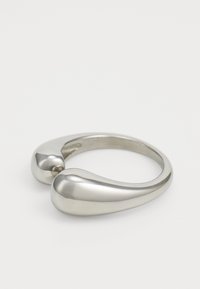Sølvfarget metallring med et glatt, buet design. Har to avrundede ender og en sømløs finish, noe som skaper en minimalistisk estetikk.