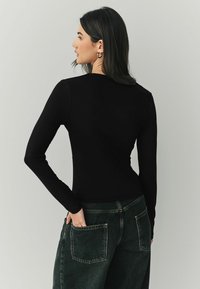 Czarny longsleeve z dopasowanym krojem, gładką fakturą i okrągłym dekoltem, zestawiony z ciemnozielonymi spodniami o szerokich nogawkach z tylnymi kieszeniami.