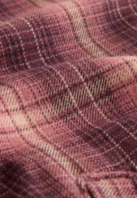 Tekstil med et ternet mønster i nuancer af pink og creme, lavet af uld med en blød tekstur, der har et vævet design og kontrasterende linjer.