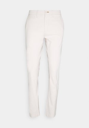 Weiße schmale Hose mit Knopfverschluss, Gürtelschlaufen sowie Seiten- und Münztaschen, vor neutralem Hintergrund präsentiert.