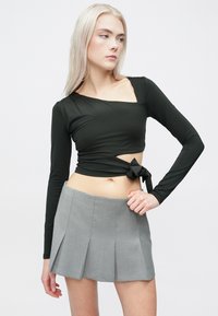 Μαύρη μπλούζα μακρυμάνικη με τετράγωνη λαιμόκοψη, με κόμπο στη μέση. Ανοιχτό γκρι μίνι φούστα πλισέ με καλοραμμένη φινίρισμα.