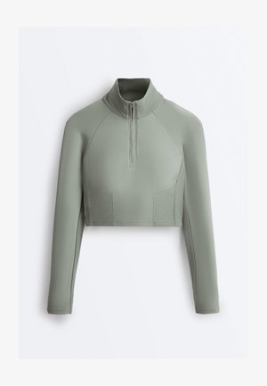 Langärmelig cropped sporttop in saliegroen met geribbelde col en zijpaneel details, voorzien van een halve ritssluiting aan de voorkant.