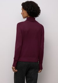 Burgundský rolák s přiléhavým střihem a žebrovaným límcem a manžetami, kombinovaný s tmavými vzorovanými kalhotami. Minimalistický styl.