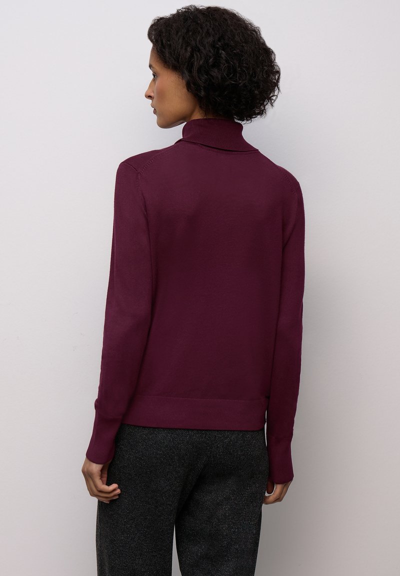 Burgundský rolák s přiléhavým střihem a žebrovaným límcem a manžetami, kombinovaný s tmavými vzorovanými kalhotami. Minimalistický styl.