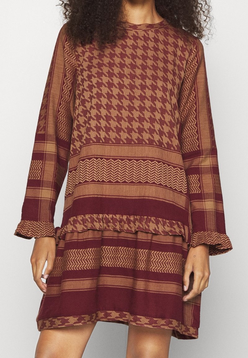 Robe à manches longues en tissu maroon et marron avec des motifs pied-de-poule et zigzag, volants au bas et coupe ample.