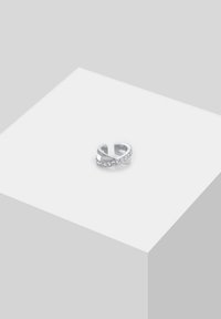 Anello d'argento con un design intrecciato e cristalli trasparenti incastonati su un lato, finitura liscia e estremità aperte regolabili.