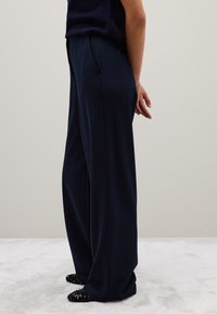 Donkerblauwe wijde broek met zijzakken en een gladde stoftextuur, gecombineerd met zwarte glinsterende instappers.