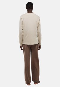 Chemise beige à manches longues avec col rond, assortie à un pantalon marron ample. Texture de tissu lisse, design minimaliste.