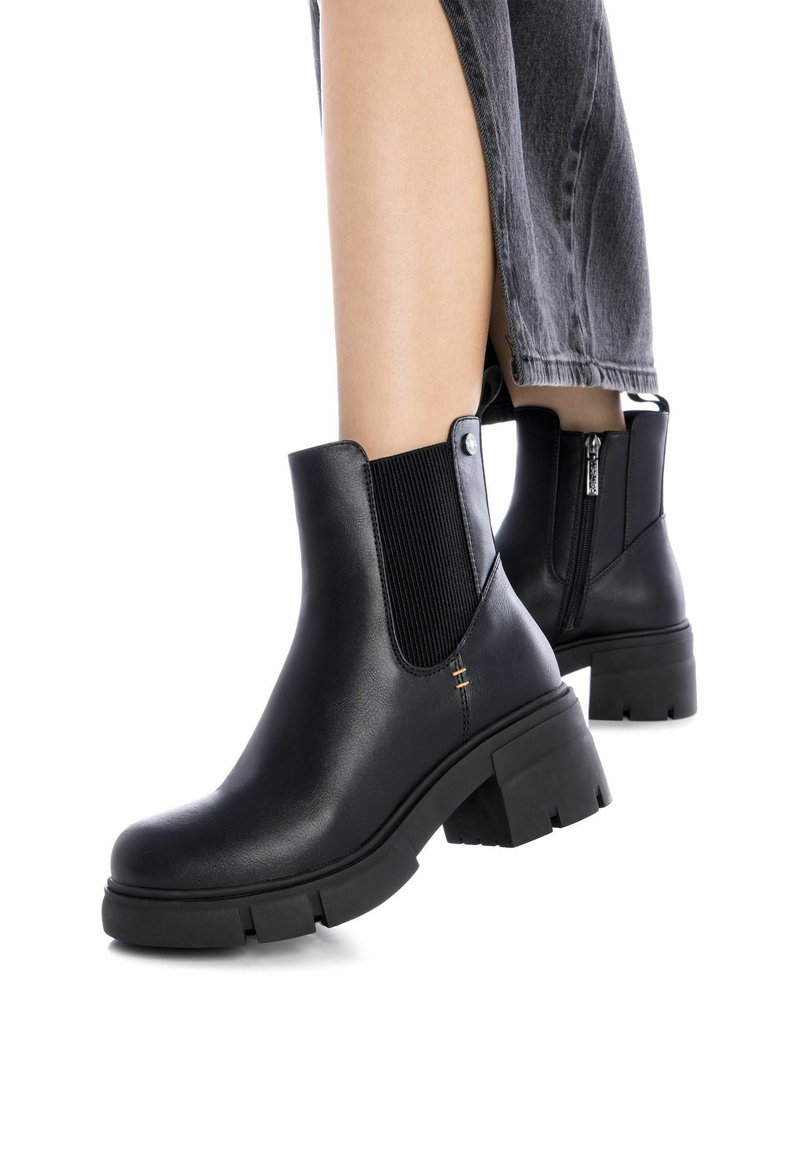 Botas de tobillo negras con un acabado de cuero suave, paneles laterales elásticos y una suela de goma gruesa. Cuenta con una cremallera lateral para facilitar su uso.