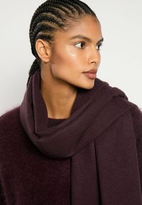 Burgundijas šalle, kas izgatavota no mīkstas, teksturētas auduma, brīvi norauta ap kaklu. Gluda, plūstoša dizaina ar vienkāršu apdari.