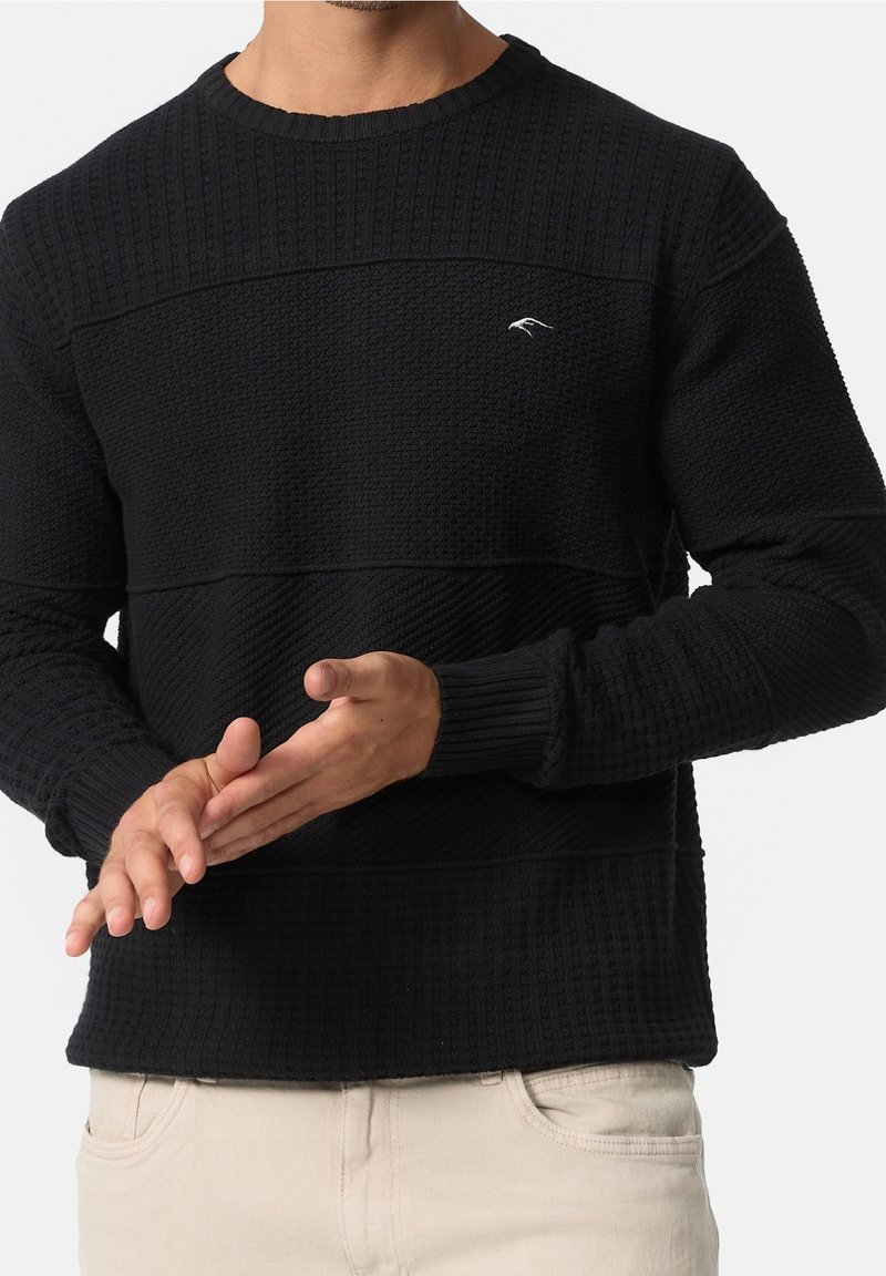 Pull noir avec tissu texturé et rayures horizontales. Poignets et ourlet côtelés. Petit logo sur la poitrine.