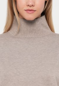 Beige ribbed turtleneck sweater with a textured finish. Features a high collar and a soft, smooth fabric that drapes gently.
