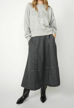 Femme portant un sweat-shirt gris "CHICAGO MOS MOSH", une jupe midi trapèze gris foncé et des bottes noires à bout pointu, mains dans les poches.