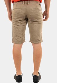 Pantaloni corti beige in cotone, con una vestibilità slim, tasche posteriori e un orlo che termina poco sopra il ginocchio. Indossati con scarpe nere.