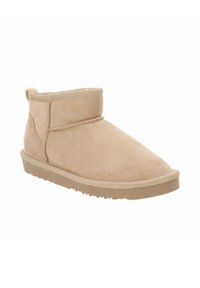 Botín tobillo en tonalidad arena, confeccionado en suave ante, con punta redonda, costuras mínimas y suela de goma plana. Presenta un cuello corto y una lengüeta.