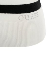 Witte gebreide beanie met een zwarte horizontale streep. Bevat het "GUESS" logo in lichtgrijs, met een geribbelde textuur aan de onderrand.
