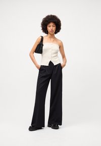 Top de malha creme sem alças com detalhes em botão e barra com franjas, combinado com calças pretas de perna larga e uma pequena bolsa preta. Sapatos de plataforma pretos.