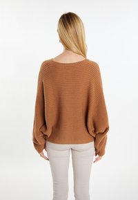 Bruine geribbelde gebreide trui met een brede halslijn en oversized mouwen, gecombineerd met beige aansluitende broek. Minimalistisch ontwerp, gezellige textuur.