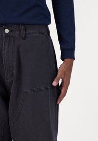 Dark gray denim cargo pants with side pockets, a straight fit, and a metal button closure. The fabric has a subtle texture.
