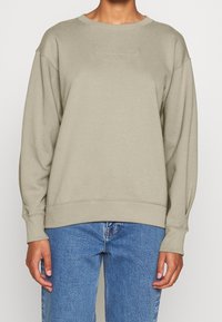 Sudadera verde oliva claro con cuello redondo y mangas largas, con un logotipo en relieve en el pecho y puños y dobladillo acanalados.