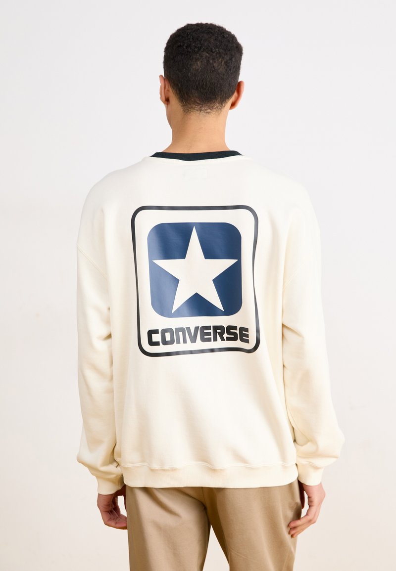 Krémová mikina vyrobená z mäkkej látky, na zadnej strane so veľkou modrou hviezdou a logom "CONVERSE". Rybárske detaily na manžetách a výstrihu.