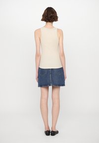 Beige ärmelloses Top, kombiniert mit einem blauen Jeansrock. Das Top ist figurbetont, während der Rock aufgesetzte Taschen und einen geraden Saum hat. Schwarze Ballerinas runden den Look ab.