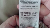 Étiquette de soin en tissu tissé, blanche avec des symboles noirs. Contient des instructions de lavage en plusieurs langues et la mention "Exclut la décoration".