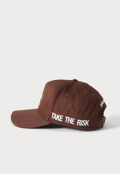 Gorra de béisbol marrón con texto blanco "TAKE THE RISK" en el lateral y correa ajustable en la parte trasera, mostrada desde el lado izquierdo.