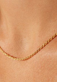 Collier en chaîne torsadée en or reposant sur la peau, présentant une texture lisse et des maillons régulièrement espacés, avec un subtil éclat métallique.