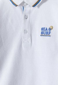 Bílá polo košile vyrobená z texturované tkaniny, s modro-hnědým pruhovaným límcem, třemi knoflíky na zapínání a vyšívaným logem "SEA & SURF".
