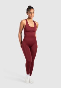 Burgunderröd ärmlös bodysuit med en figurnära design, slät textur och rundad neckline, i kombination med vita sportskor.